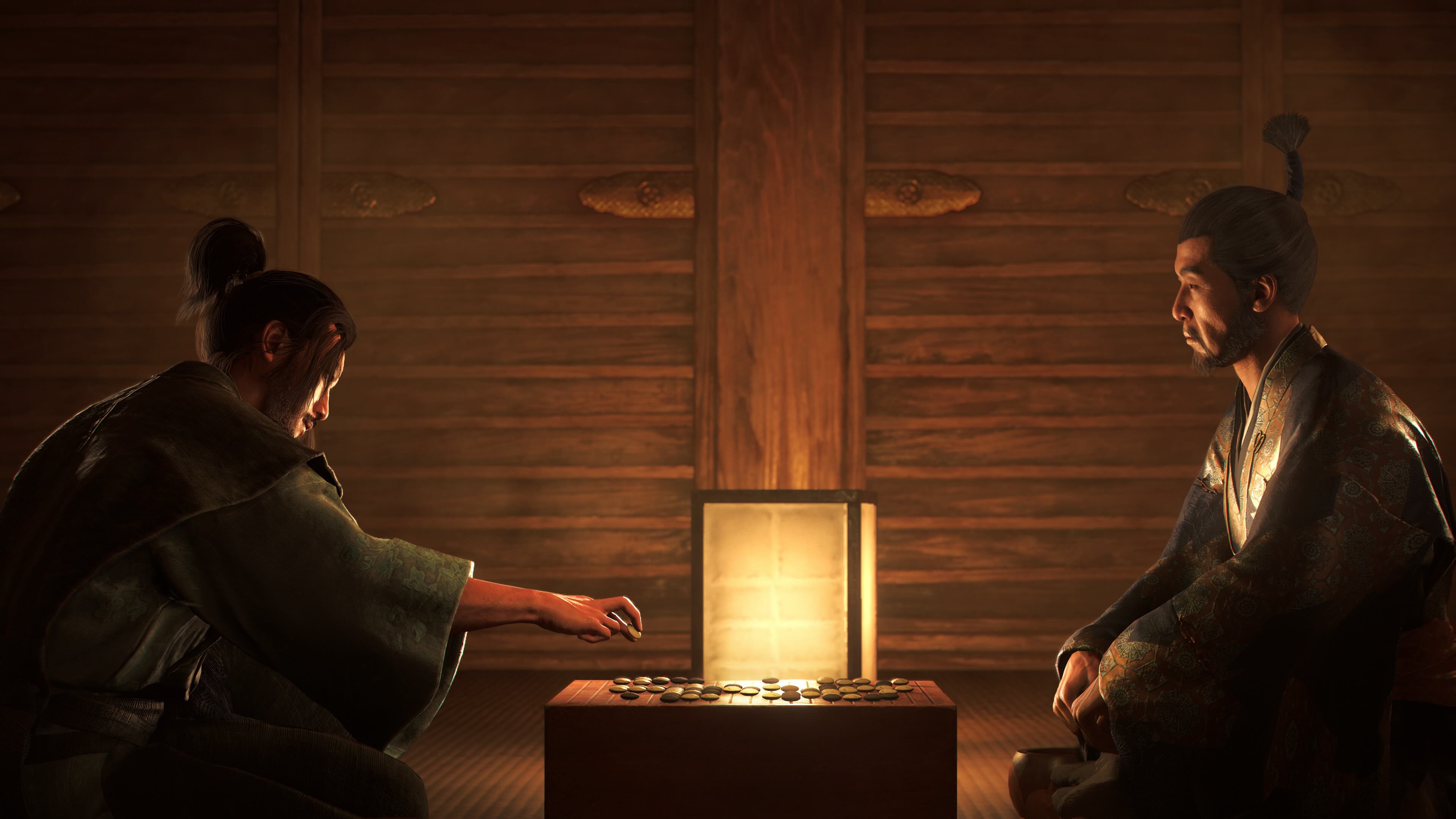 Two characters sit at a small table in a dimly lit room in Assassin’s Creed Shadows