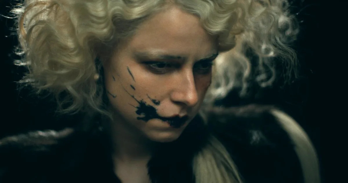 Jessie Buckley wearing a white wig with black lipstick smeared across her cheek in a promo photo for The Bride!