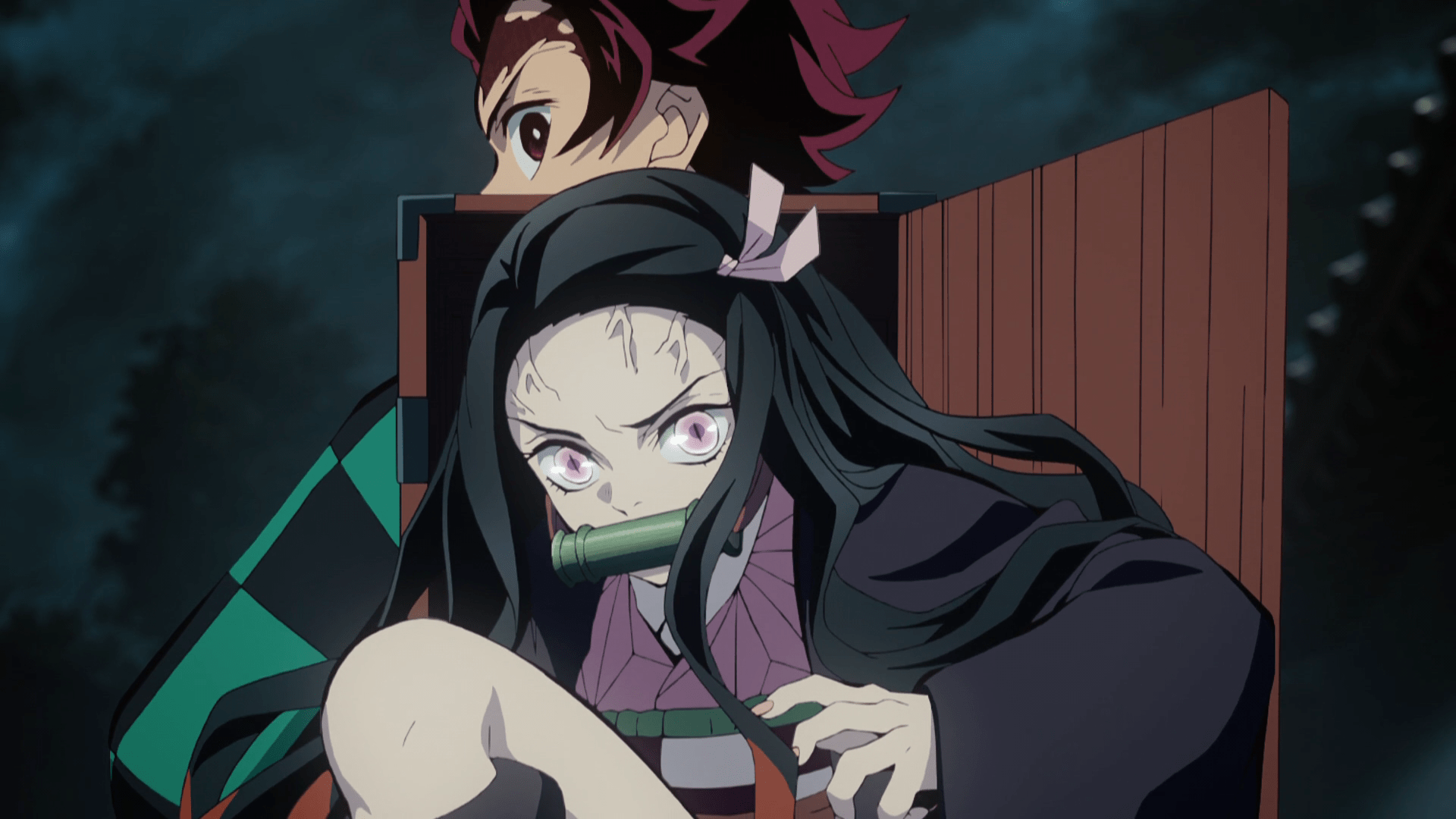 A long-haired girl with veins on her head comes out of a box that is slung around a young boy’s back
