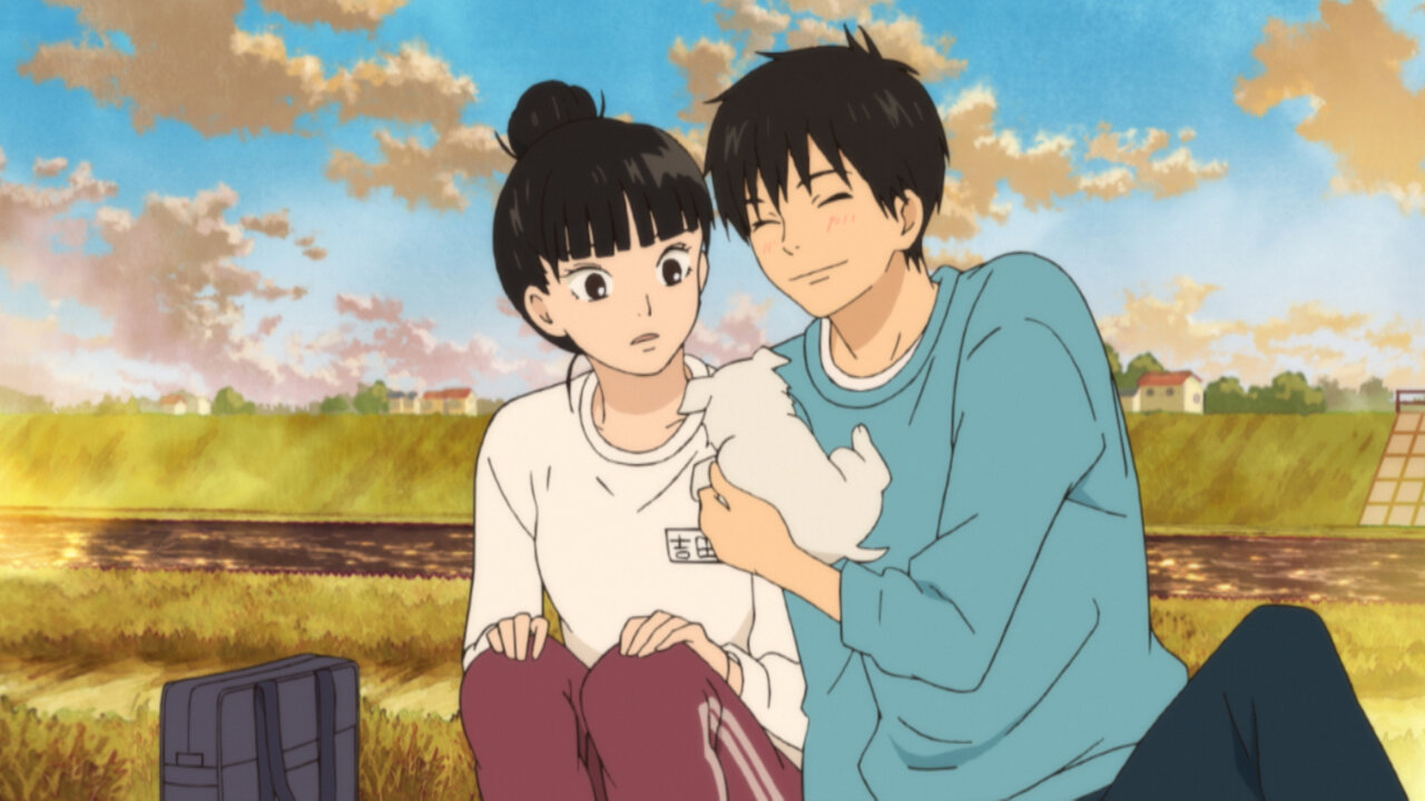 A young couple sitting next to each other on the country side in Kimi ni Todoke: From Me to You. One holds up a little puppy to the other, who is surprised