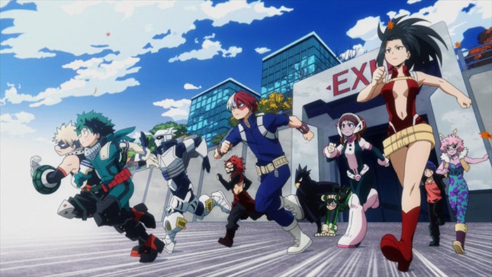 A group of costumed heroes, led by series protagonists Izuku “Deku” Midoriya&nbsp;and Katsuki Bakugo, racing out of a gate marked “Exit” to participated in a hero training exercise.