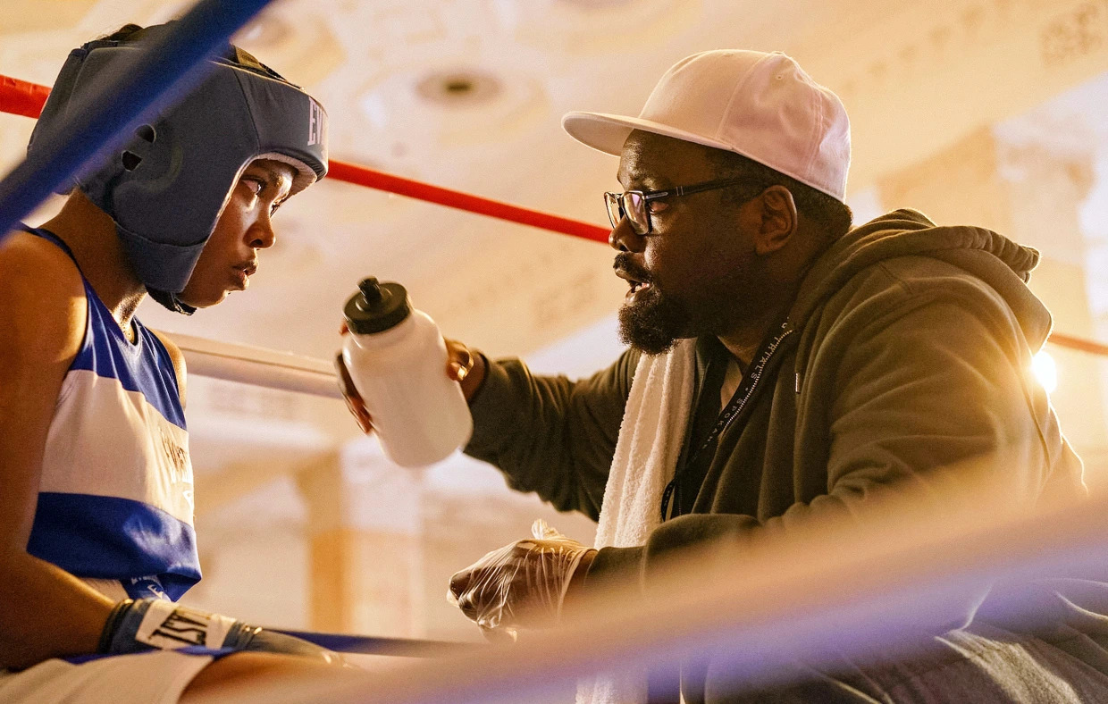 A young girl in boxing attire sitting across from her coach holding a water bottle in The Fire Inside.