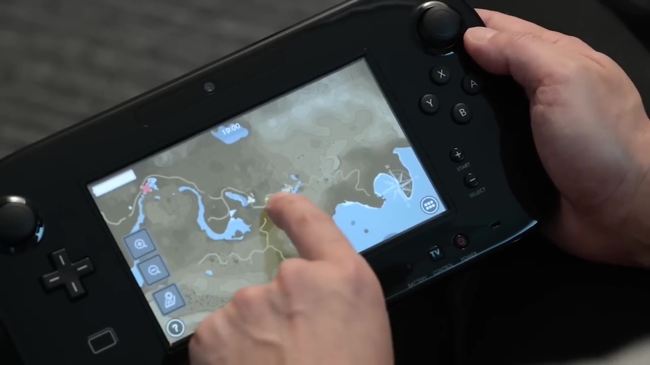 A Wii U Gamepad displaying the map from Zelda: Breath of the Wild; a hand holds the Gamepad and another points at the screen