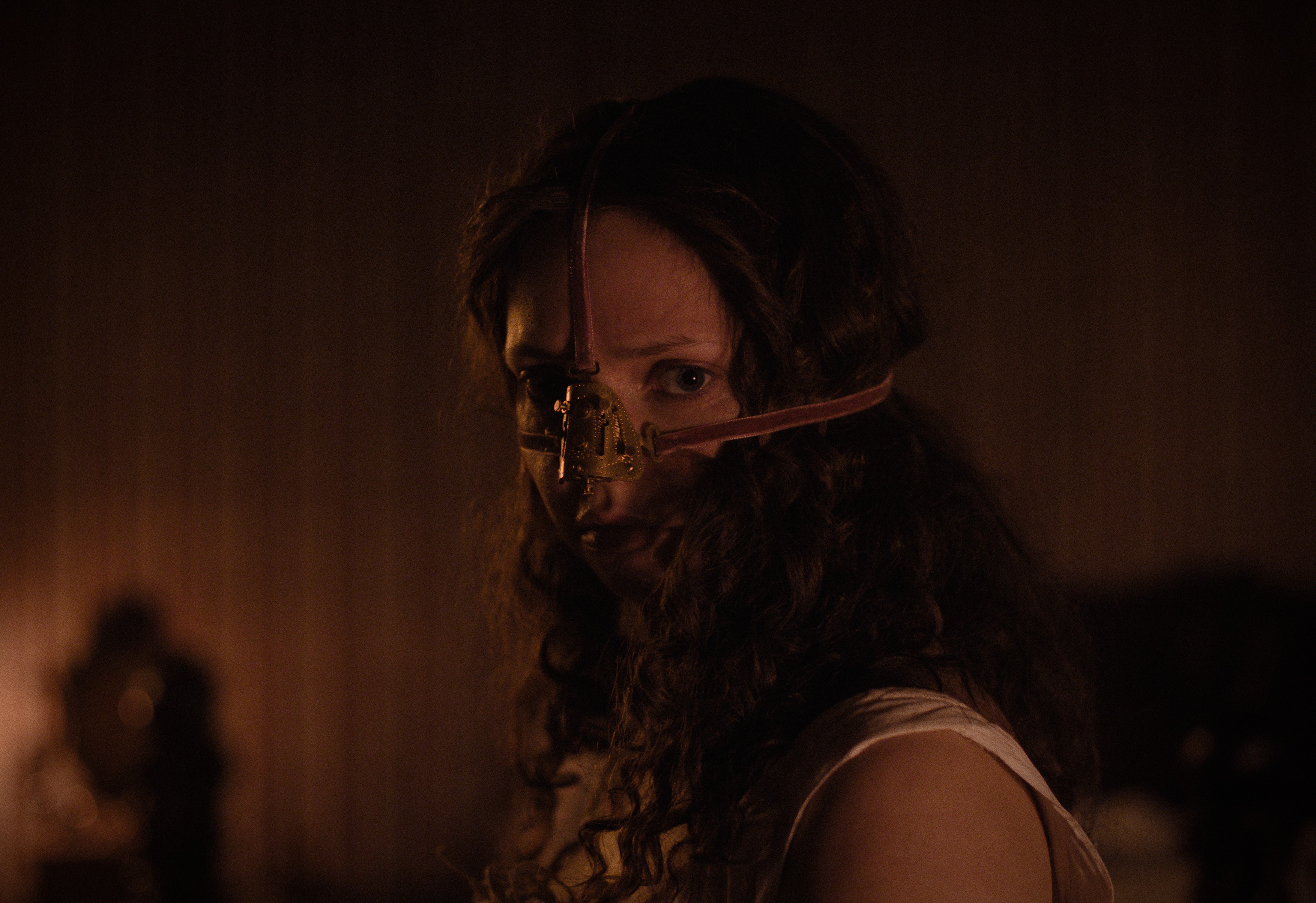 Cinderella equivalent Elvira (Lea Myren) stands in a dark room with red lighting, wearing a nose-correcting device strapped across her face in The Ugly Stepsister