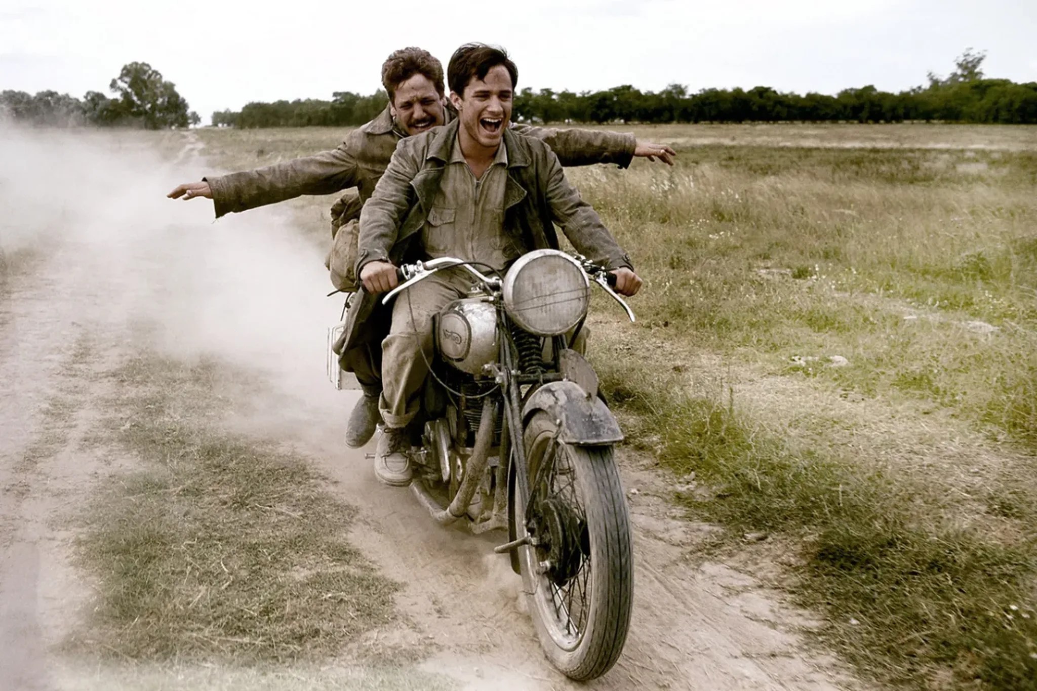 Two men laughing and riding aboard a motorcycle in a field in The Motorcycle Diaries.