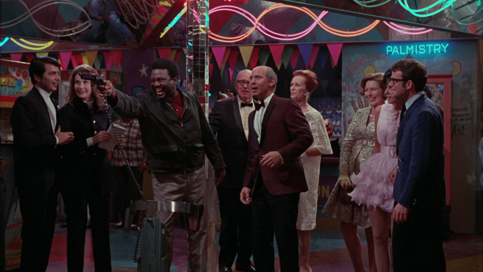 A man shooting a fake gun at a carnival while surrounding by smiling onlookers in Uptight.