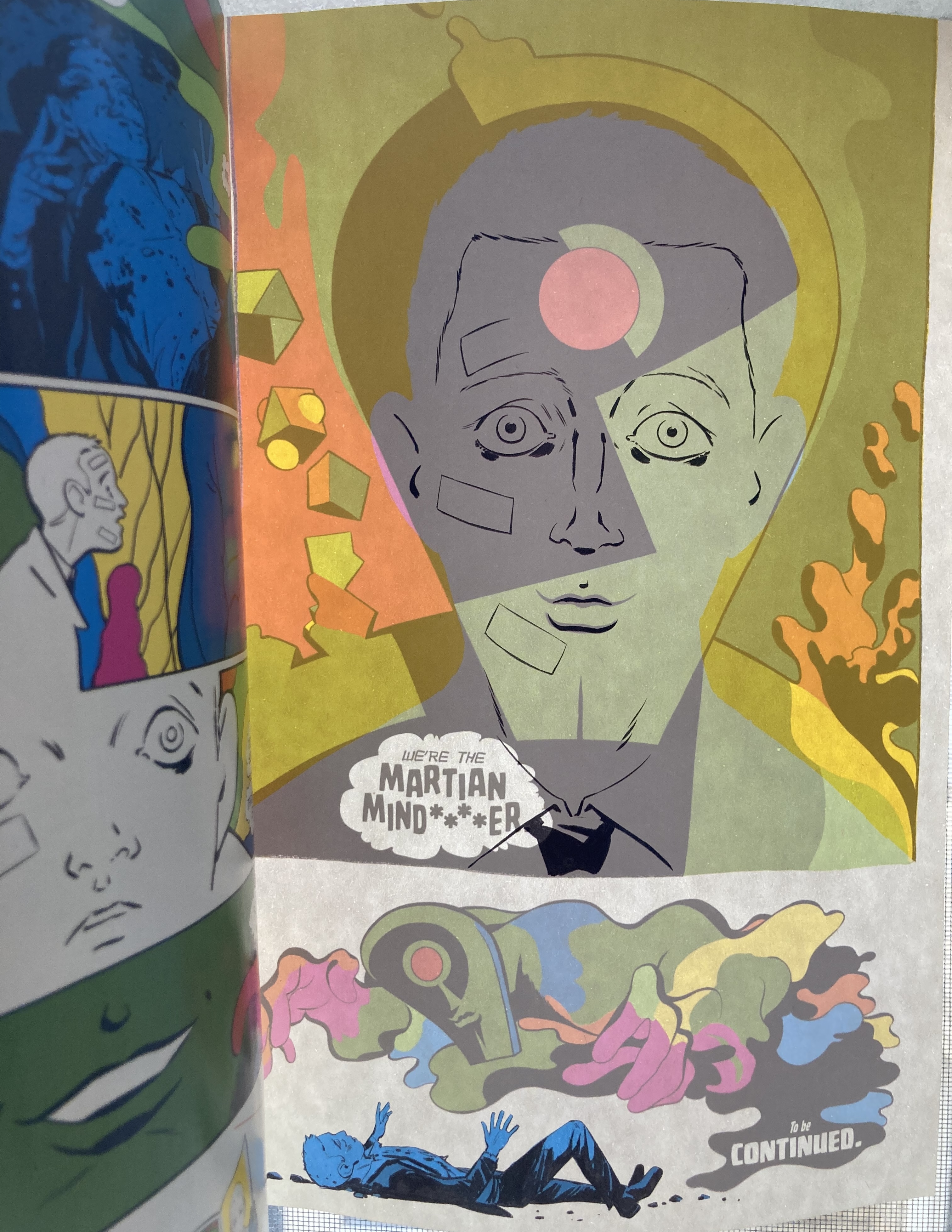 A photo of the penultimate page of Absolute Martian Manhunter #1, held up to the light so that the page printed on the reverse side of it shows through the paper, merging both images into a composite drawing of John Jones and the Martian Manhunter, and a panel of the Martians smoky form looming over John’s supine body, and flipping the second page’s mirrored text.