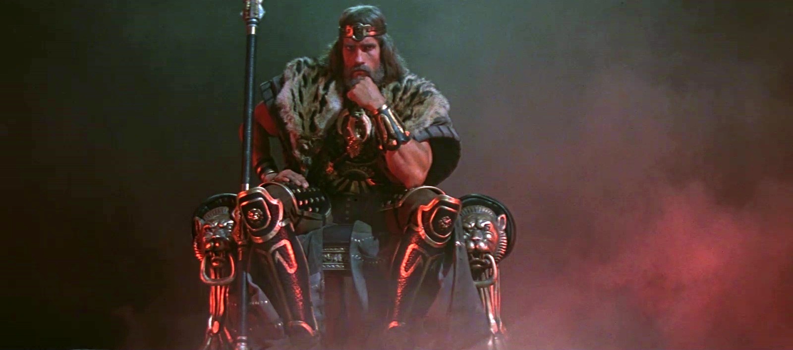 Arnold Schwarzenegger as an older Conan the Barbarian, seated on a golden throne in armor in Conan the Barbarian.