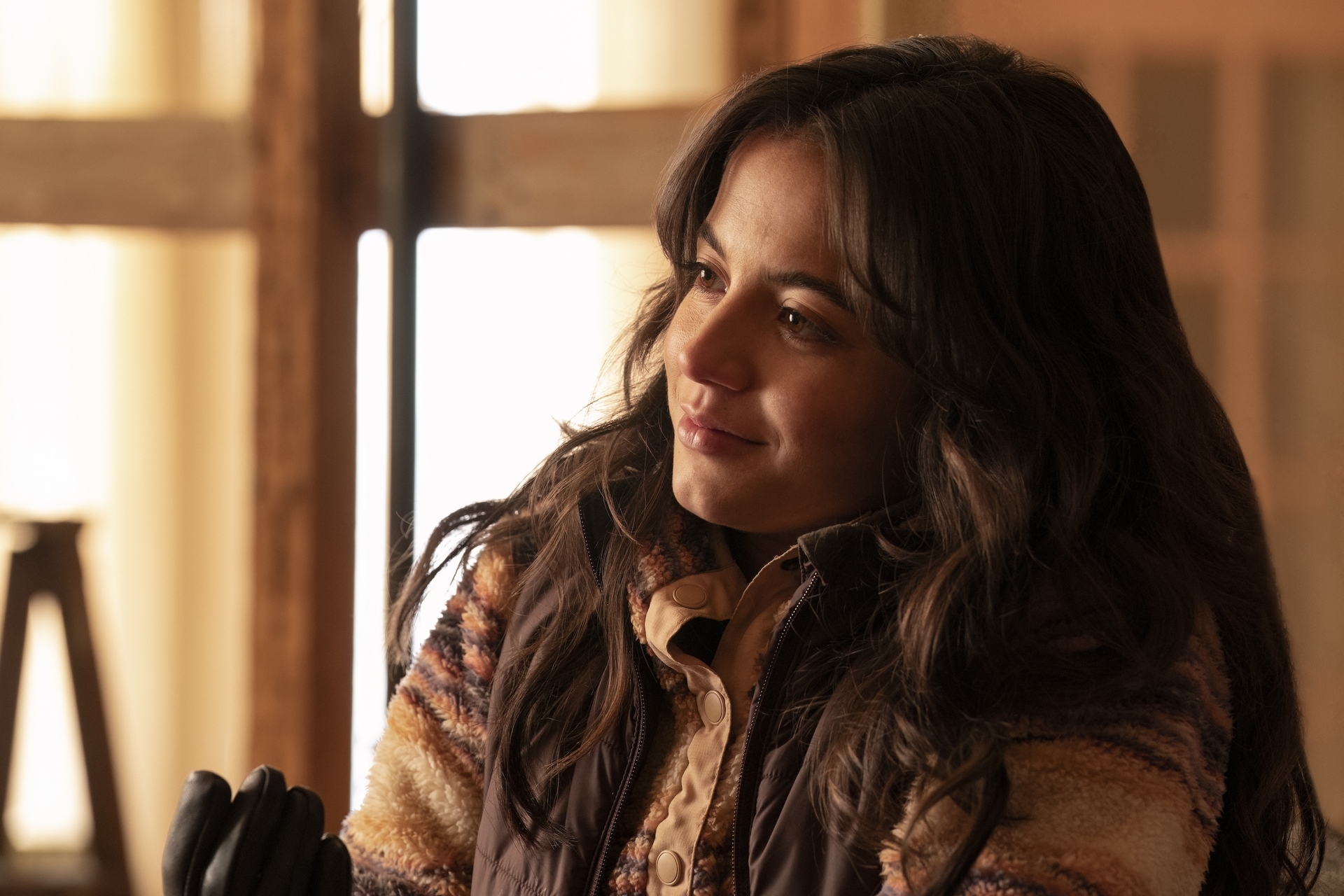Isabela Merced as Dina in The Last of Us season 2 wearing a jacket in a sunny room