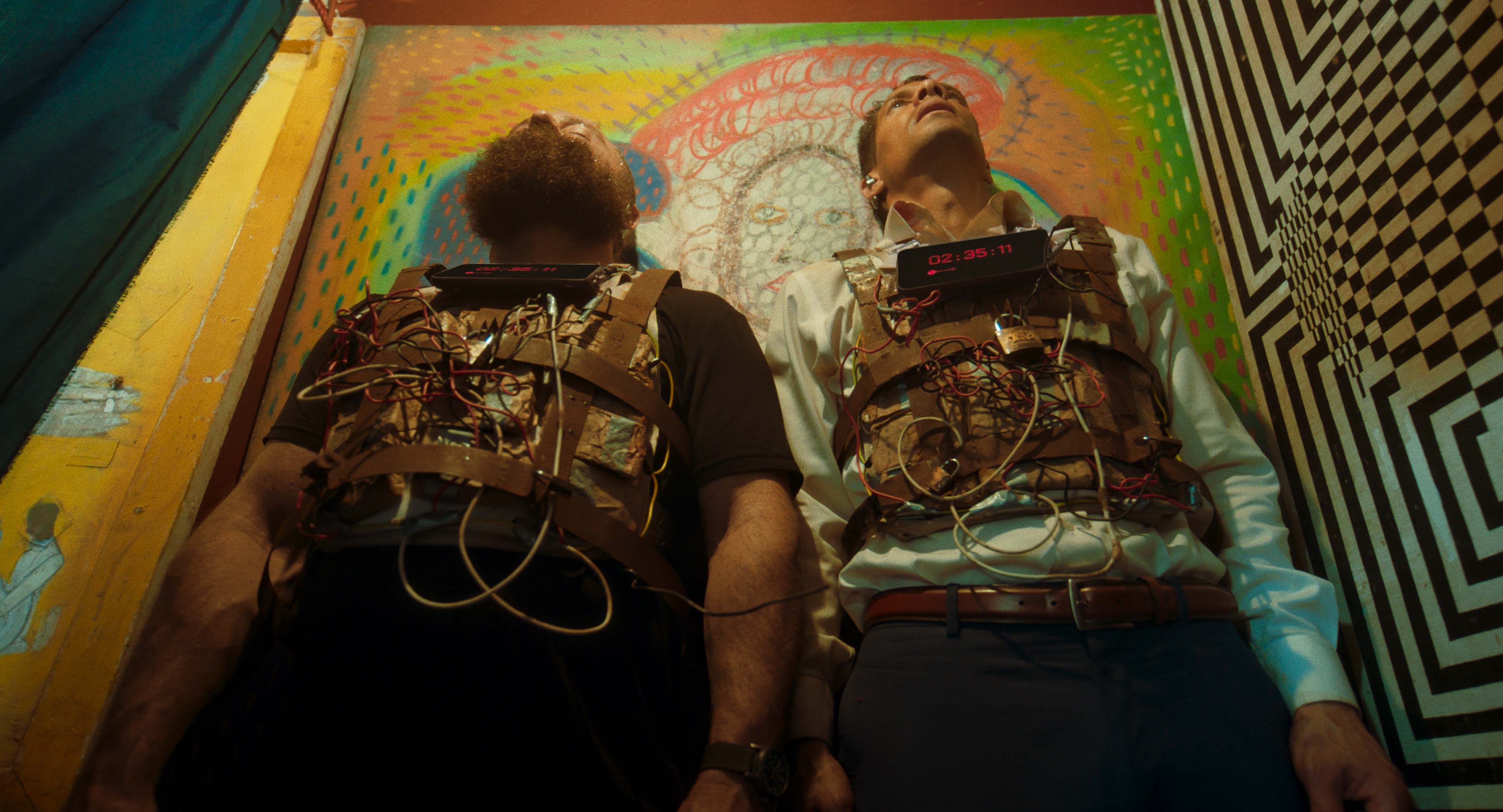 In Zero, Hus Miller and Cam McHarg stand next to each other in a small room, with bomb vests on their chests