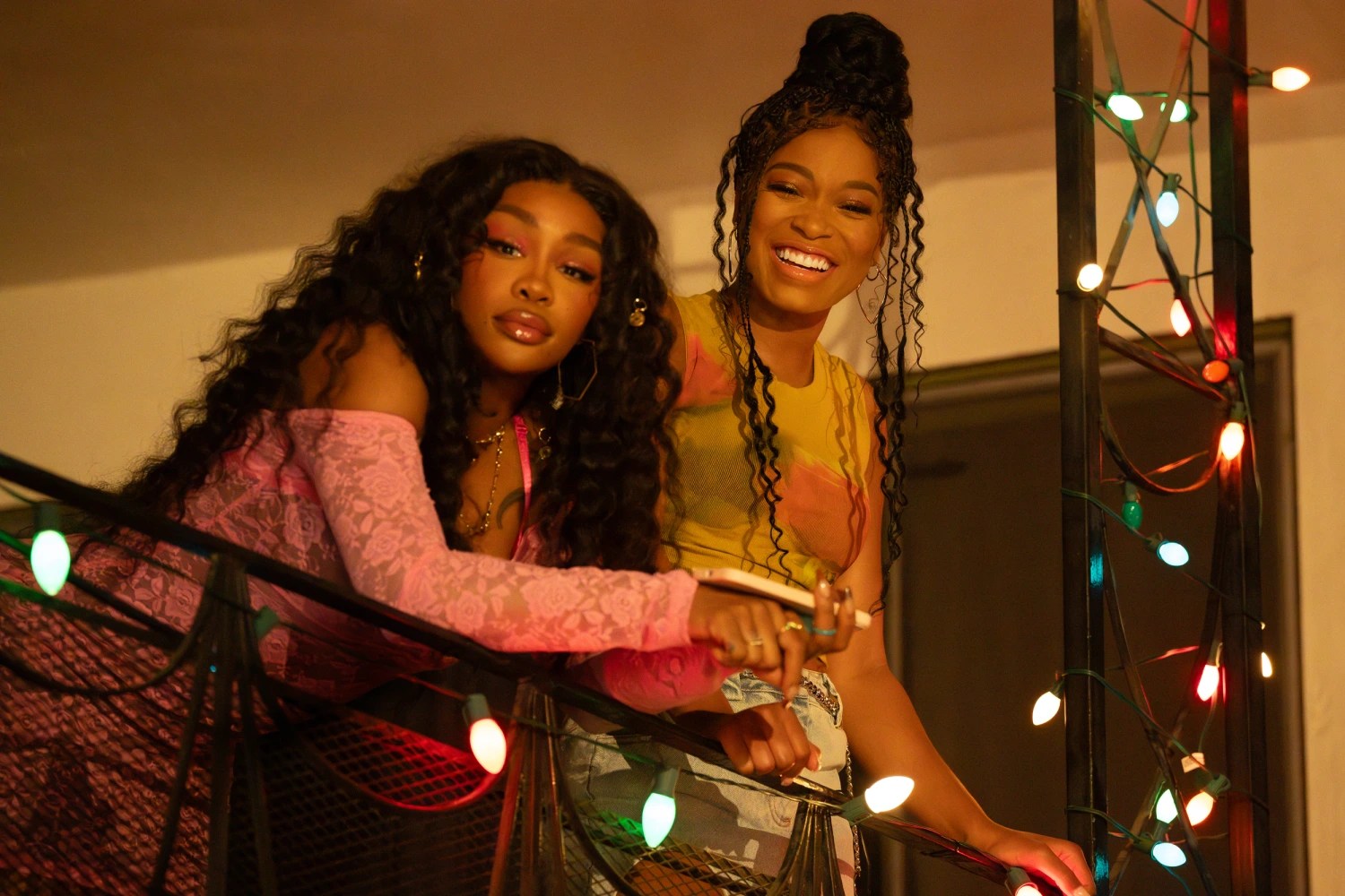 SZA and Keke Palmer leaning over a balcony decorated with christmas lights in One of Them Days.