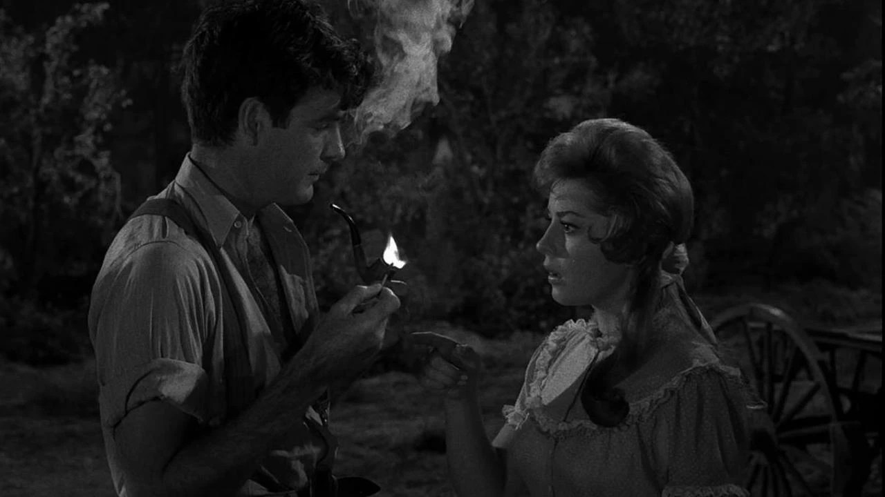A woman staring in astonishment at a man lighting his pipe with a lit match in The Last Rites of Jeff Myrtlebank, an episode of The Twilight Zone.