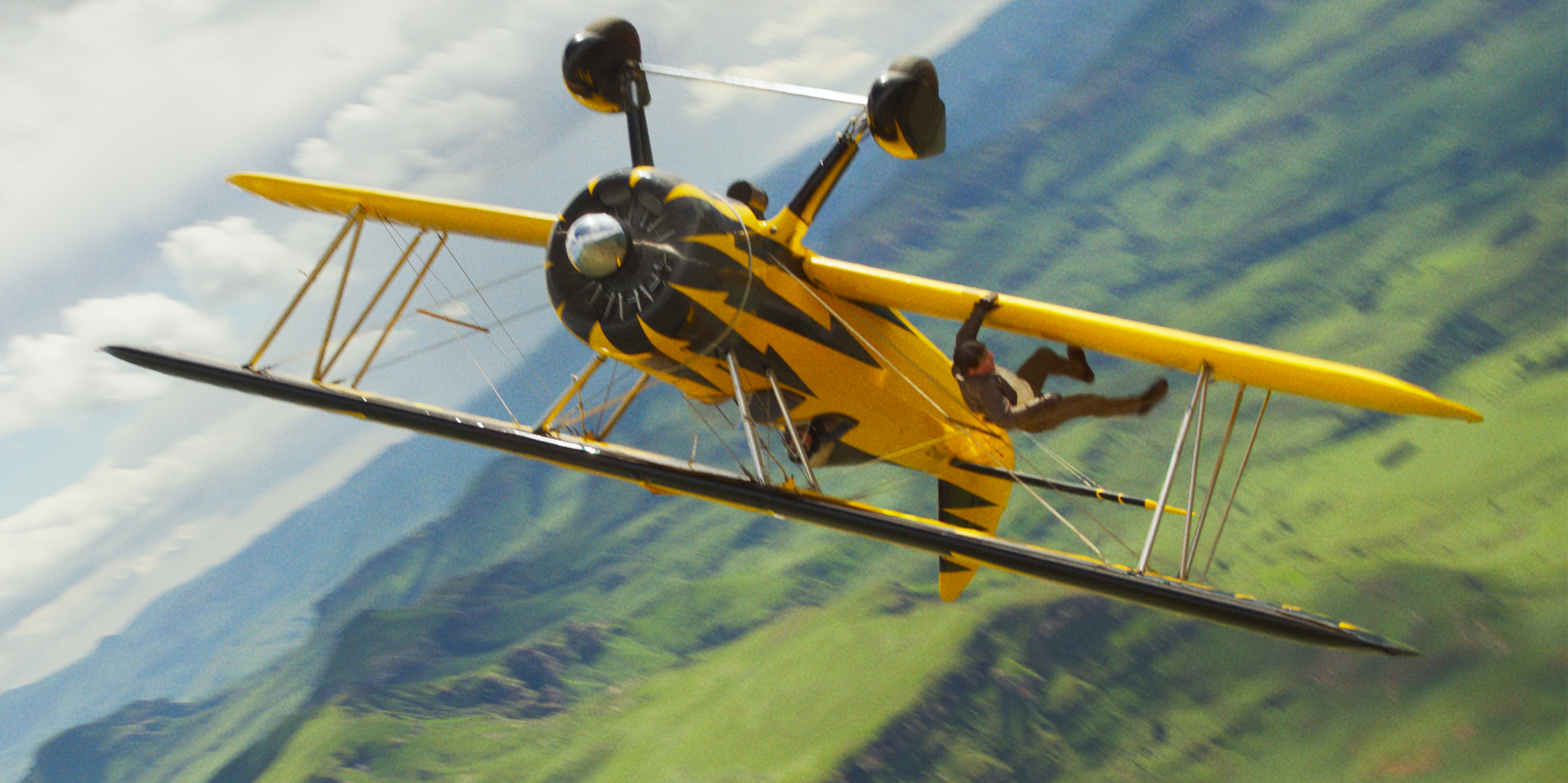 Ethan Hunt (Tom Cruise, and you can’t tell in this image, but given how he works, it’s probably really him) clings to the wing of an upside-down biplane high above the ground in Mission: Impossible — The Final Reckoning