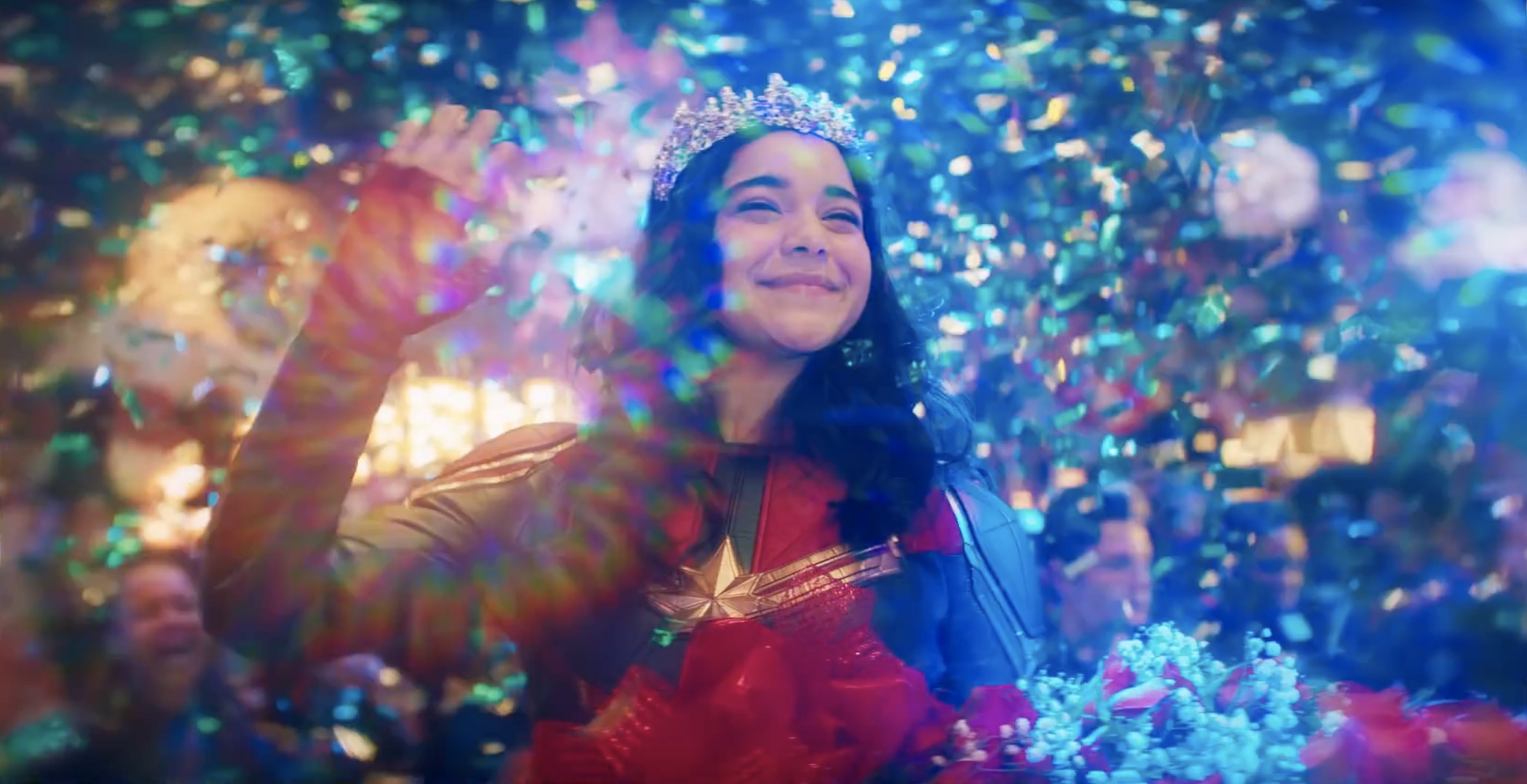 Kamala Khan waves in her Ms. Marvel costume as bright lights and confetti sprays around her