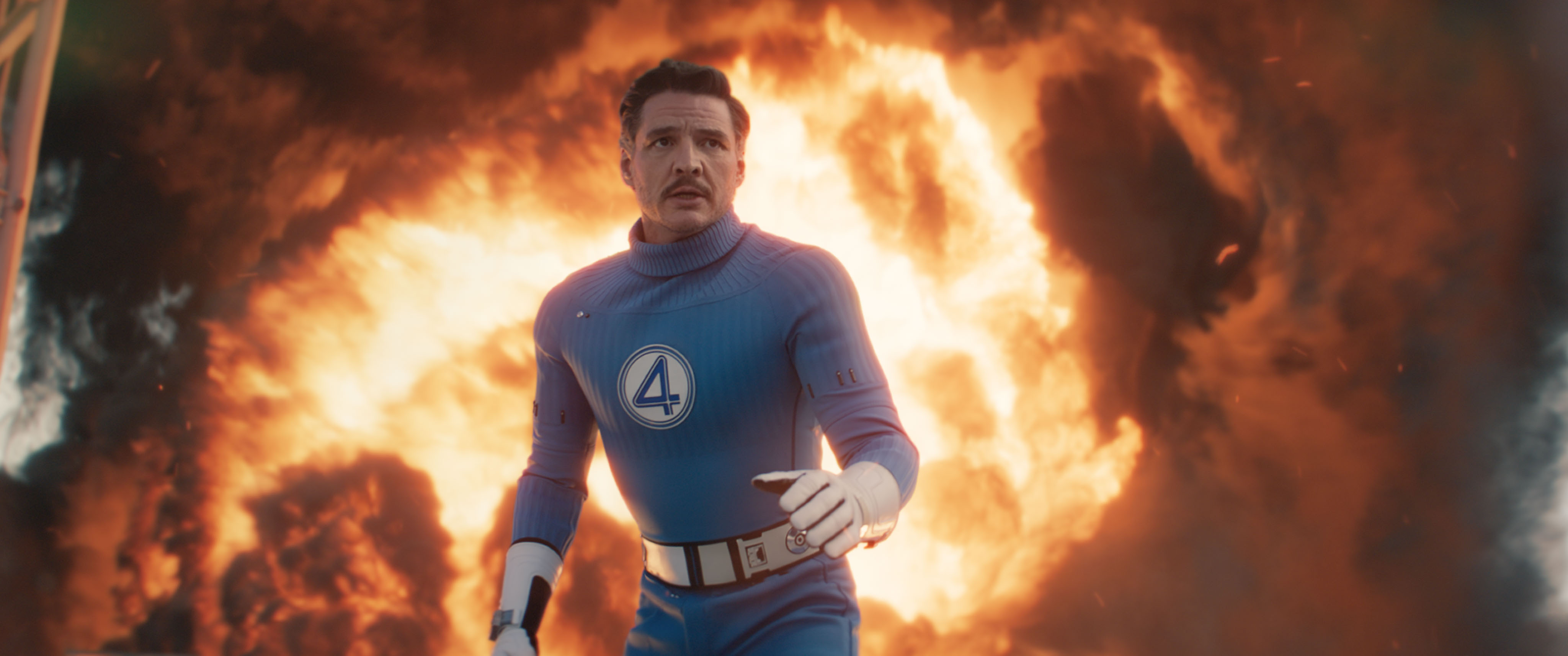Reed Richards (Pedro Pascal), in costume as Mister Fantastic of the Fantastic Four, runs toward the camera as something blows up behind him in a gout of flame in Fantastic Four: First Steps